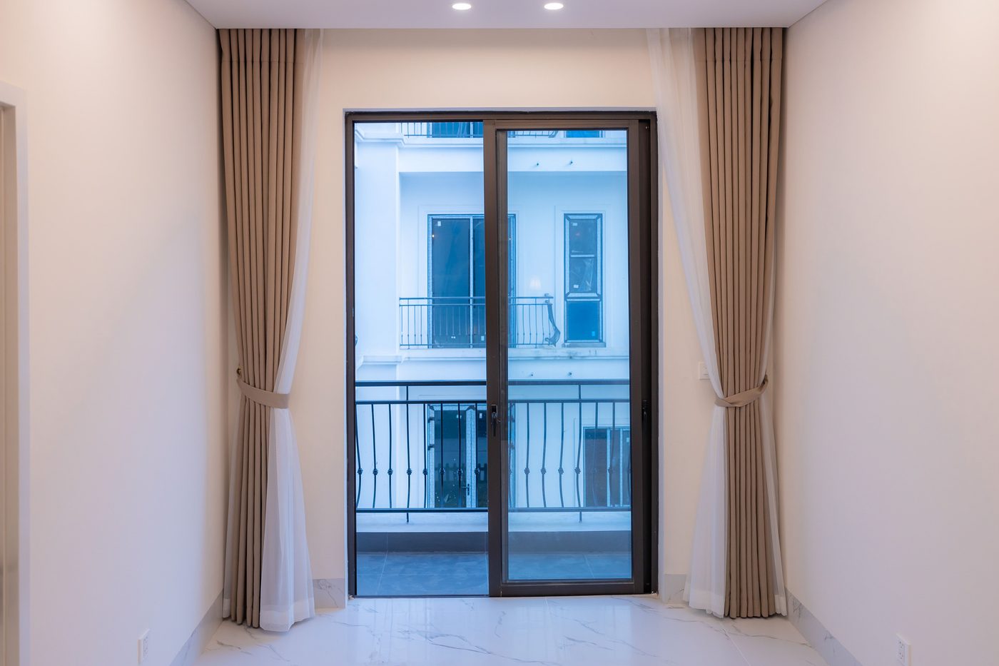 Vom Fensterbauer montierte, bodentiefe Schiebetür mit dunklem Rahmen und Blick auf den Balkon mit schmiedeeisernem Geländer